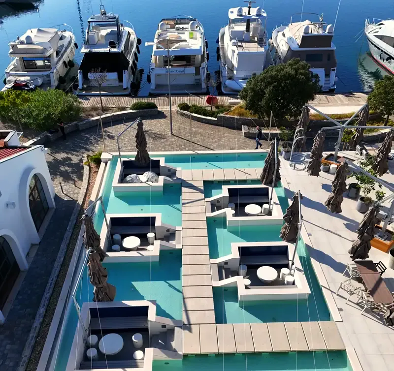 Pogled dronom na ugostiteljski bazen s ležaljkama uz marinu